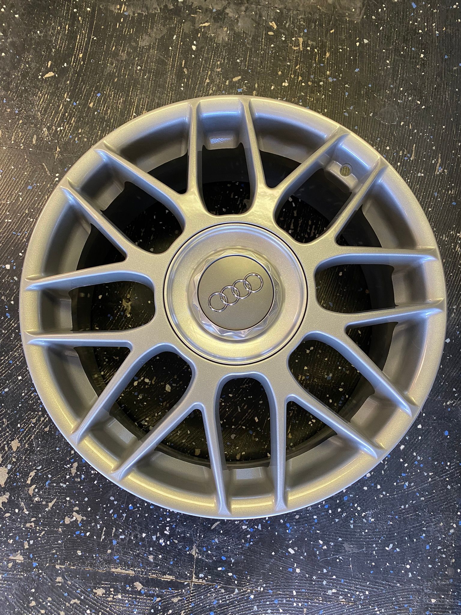 A silver audi wheel is sitting on a black surface.