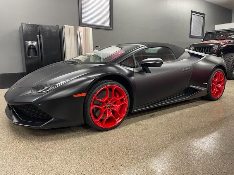 A black lamborghini huracan with red wheels is parked in a garage.