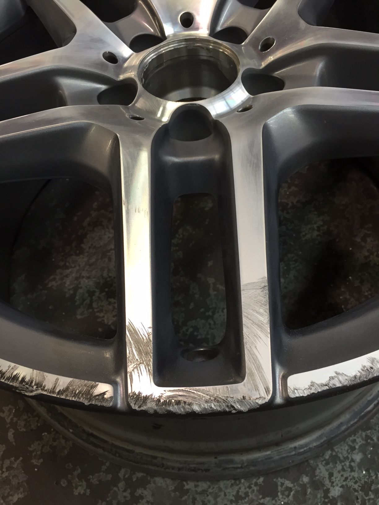Damaged silver car wheel with significant scuffing and paint chipping around the rim's edge.