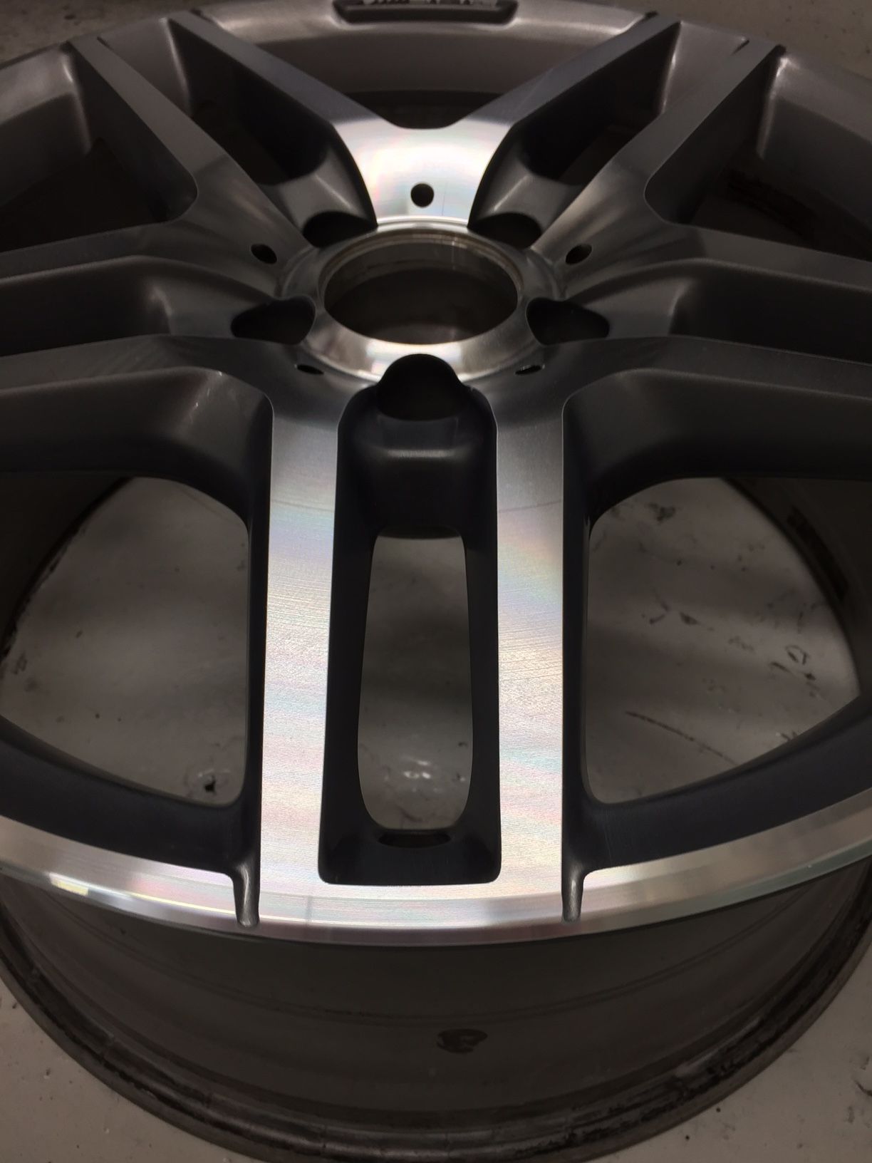 Close-up view of a silver alloy car wheel with multiple spokes and a central hub. The wheel has a metallic finish.