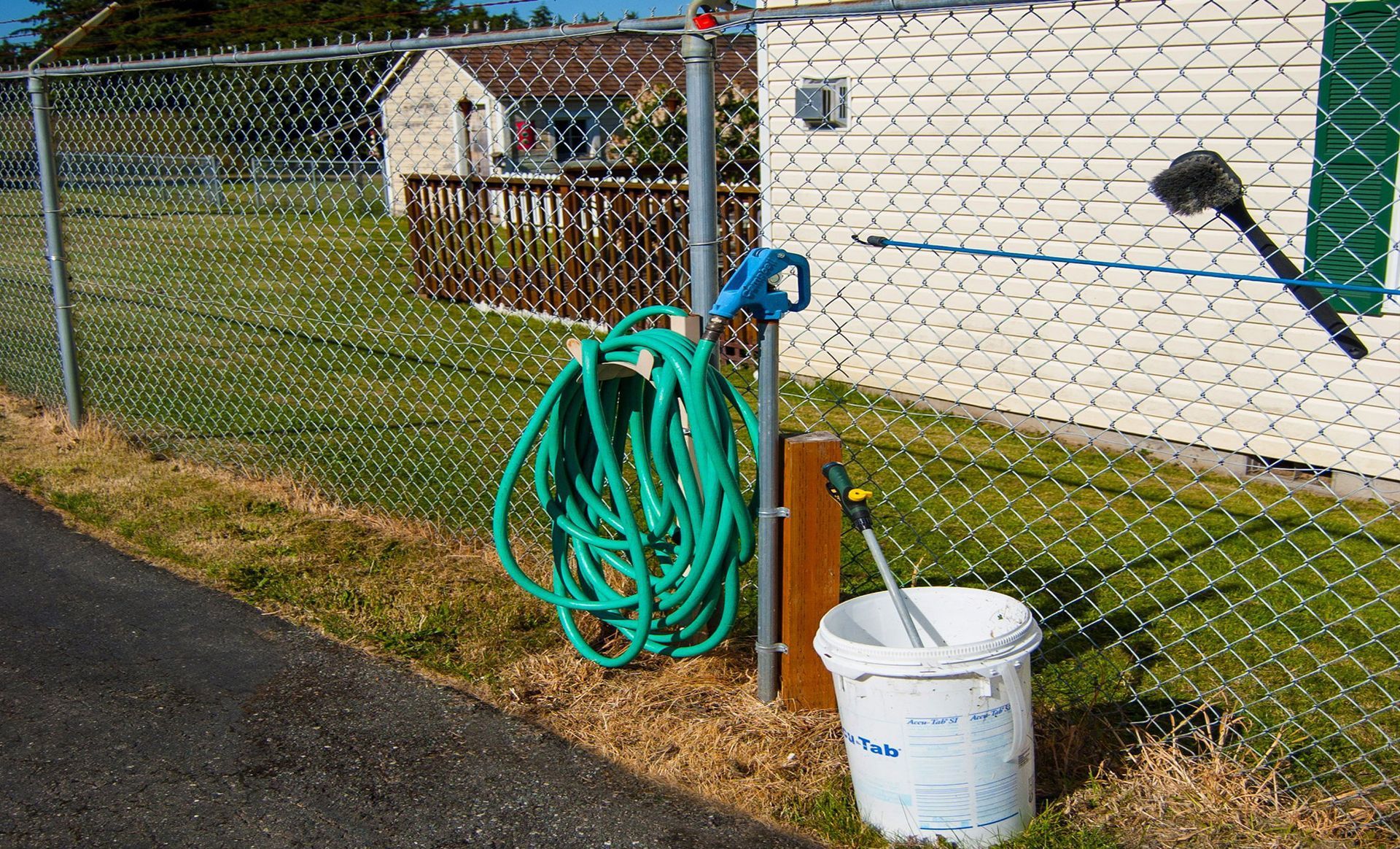a green hose is hanging on a chain link fence next to a white bucket