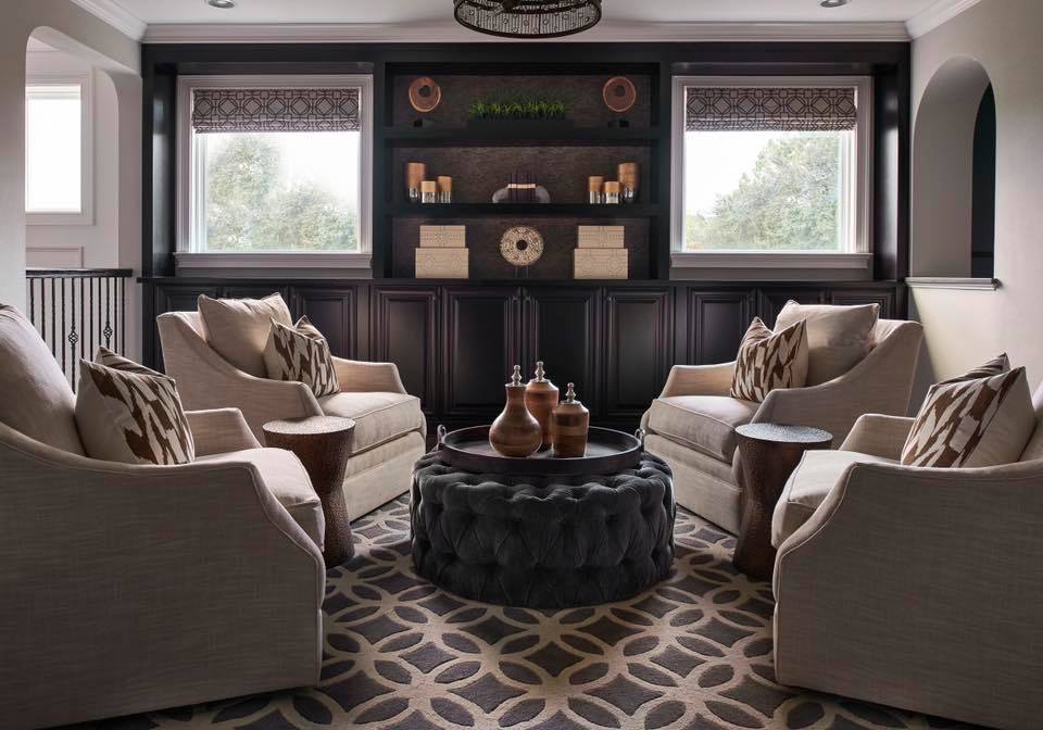 Cozy sitting area with four armchairs around a circular table, dark wood shelving and windows, patterned carpet.
