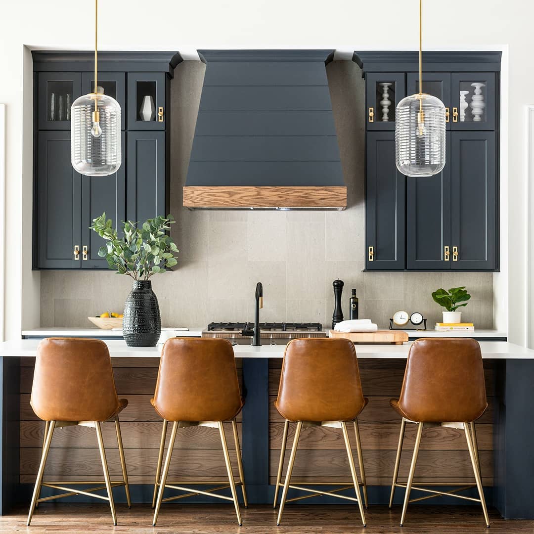 Modern kitchen with navy cabinets, a rustic hood, and leather bar stools.