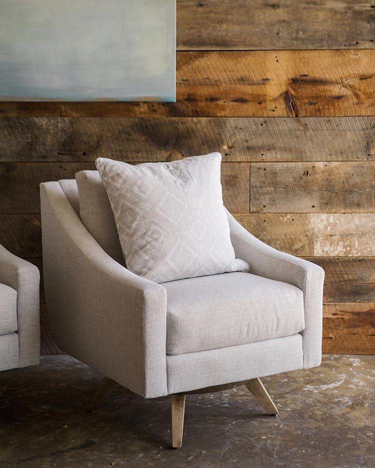Beige swivel armchair with pillow, against wooden wall, near a painting.