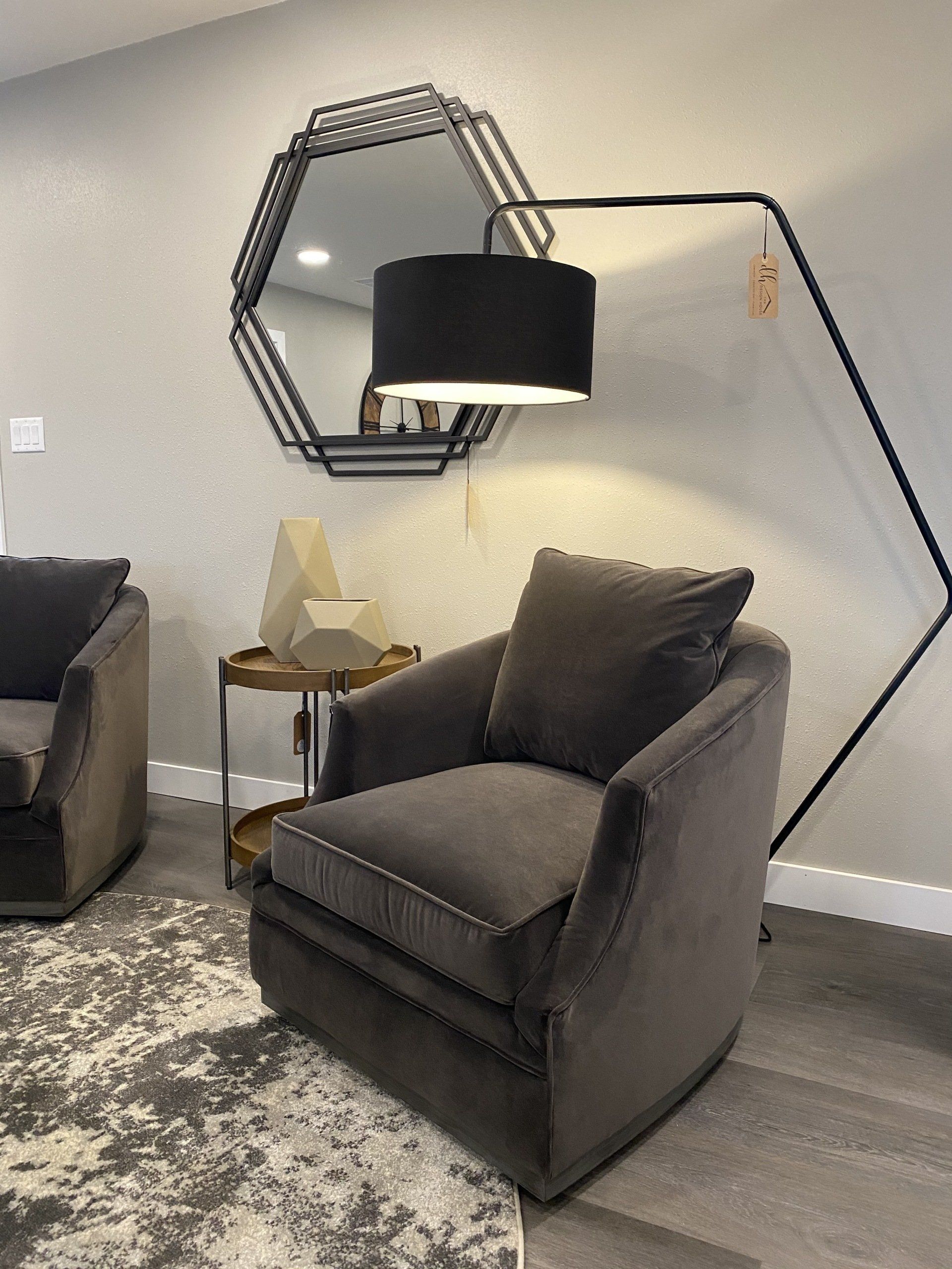 Gray armchair with throw pillow, modern black lamp, hexagonal mirror, gold side table.