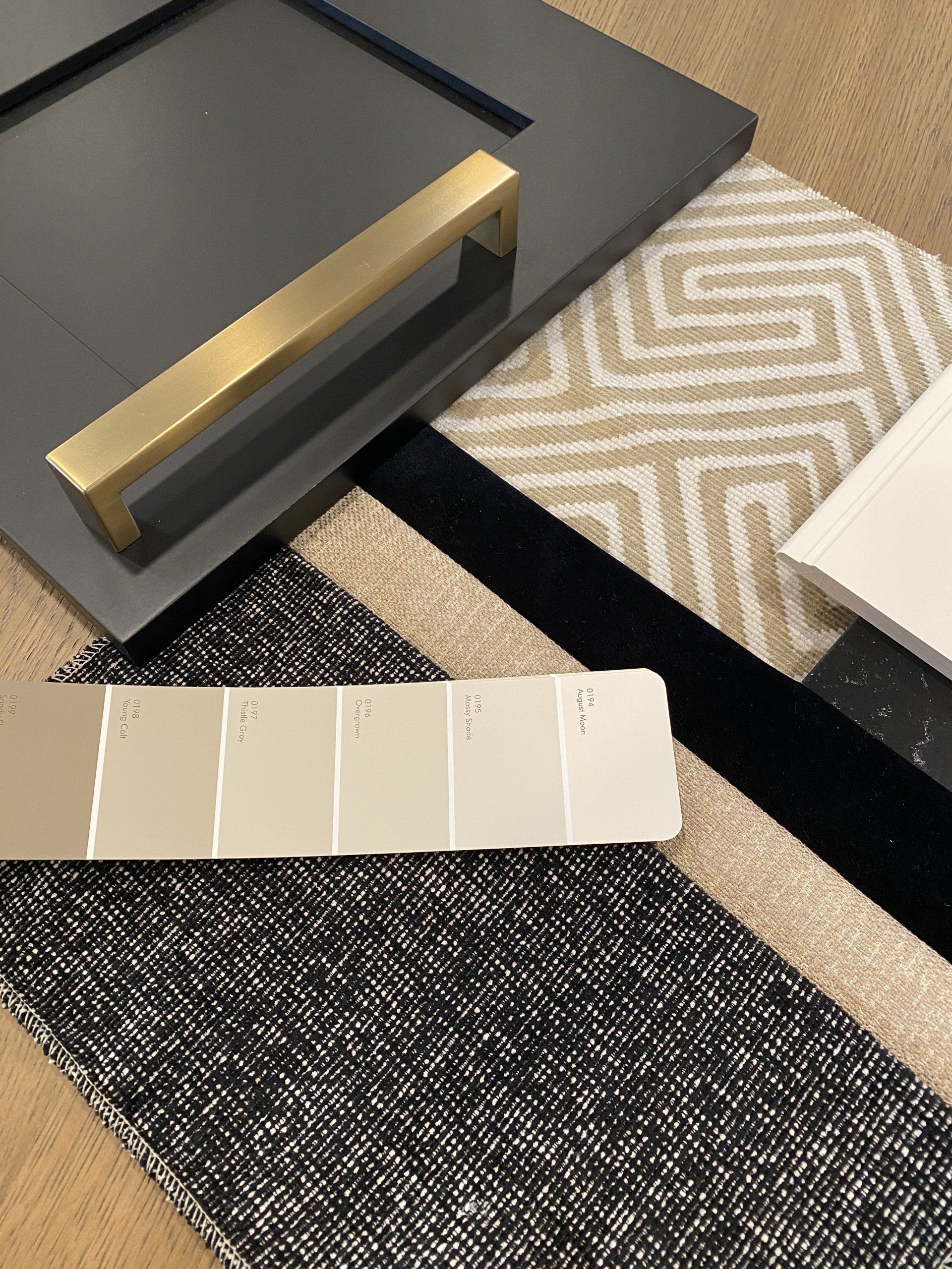 Cabinet door, gold handle, neutral carpet swatches, paint samples in varying shades of beige and gray.