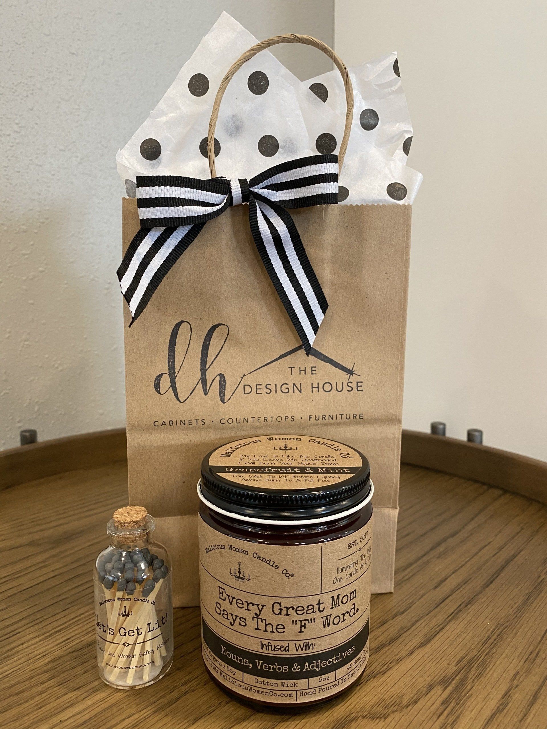 Gift bag with candle and matches on a wooden table. Brown bag with bow, polka dot tissue, and a large jar candle.
