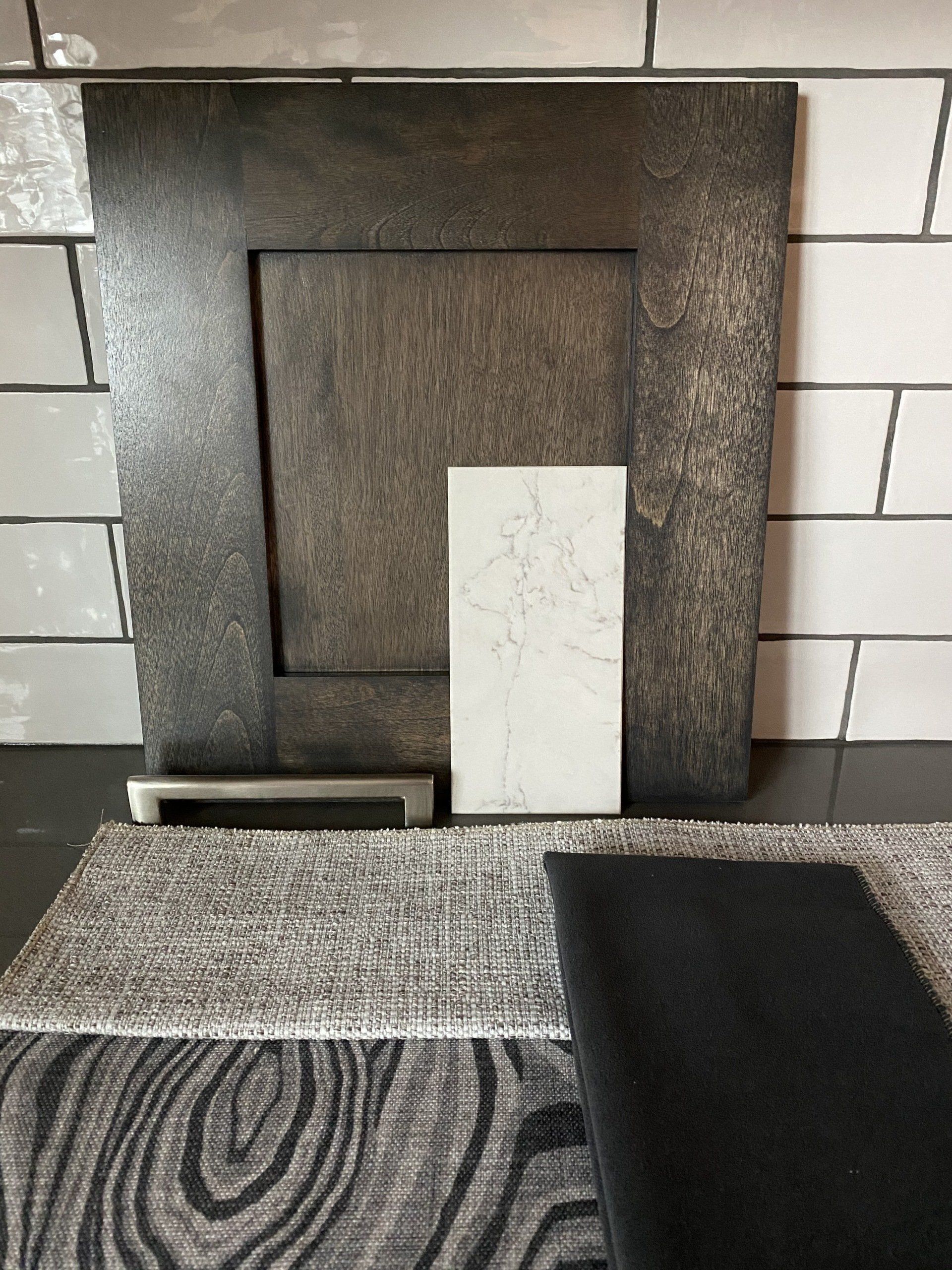 Dark wood cabinet door and fabric samples against white tile.
