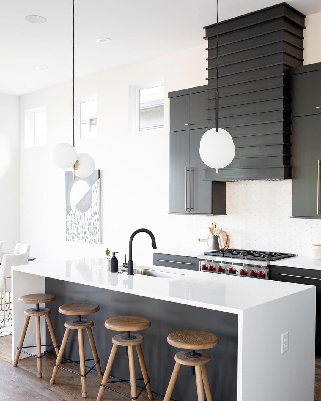Modern kitchen with white countertops, dark grey cabinets, wooden stools, and a black range hood.