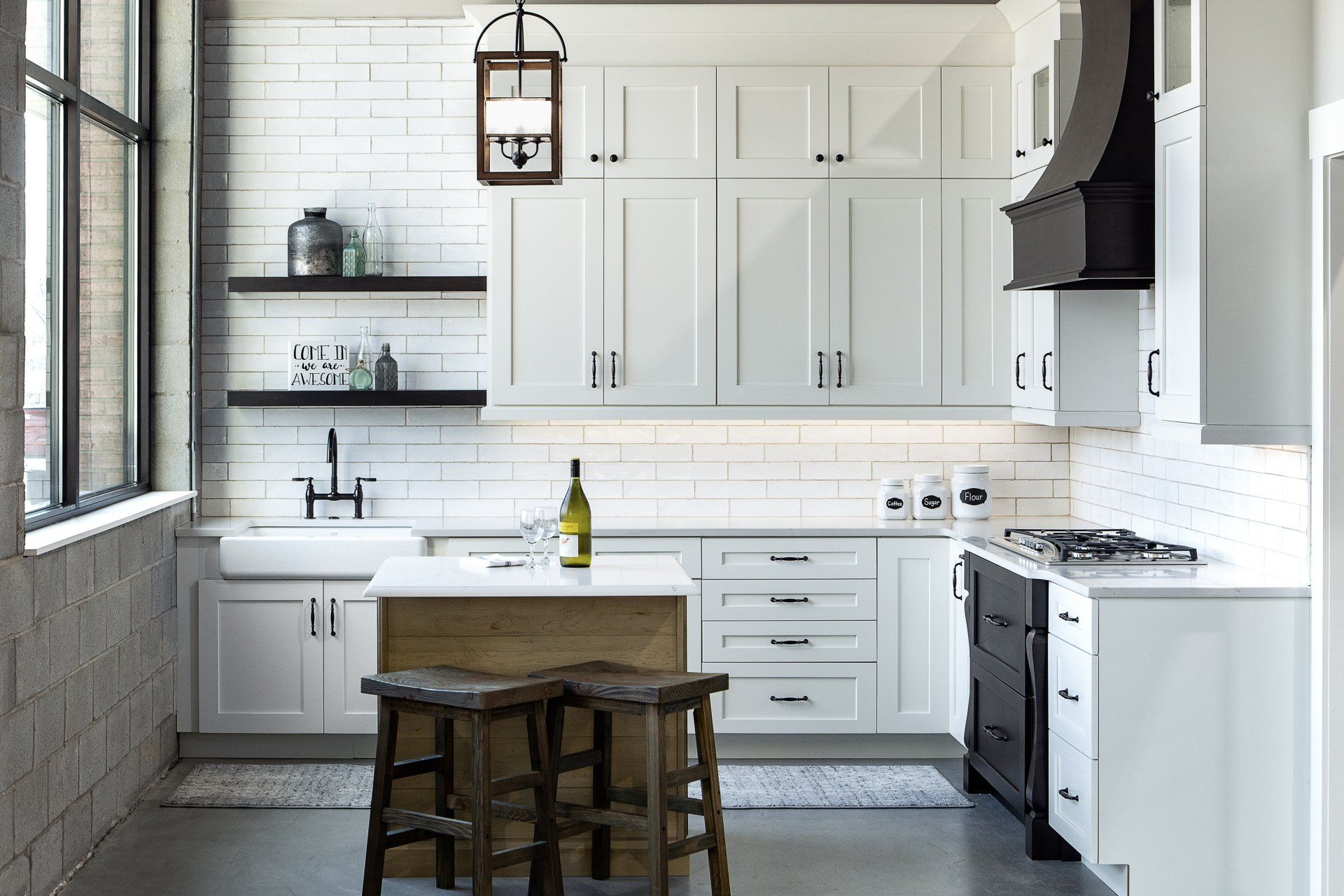 White kitchen with brick wall, island with stools, and black range.