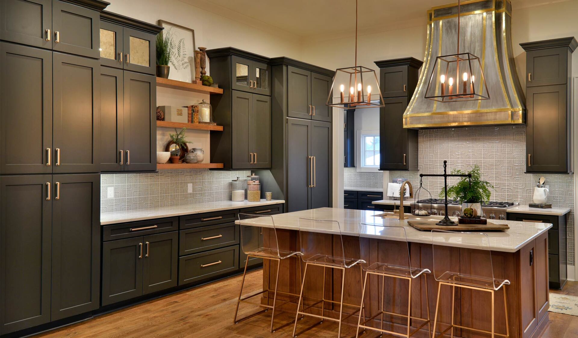 Dark green kitchen with marble countertops, gold accents, and a wooden island with clear chairs.