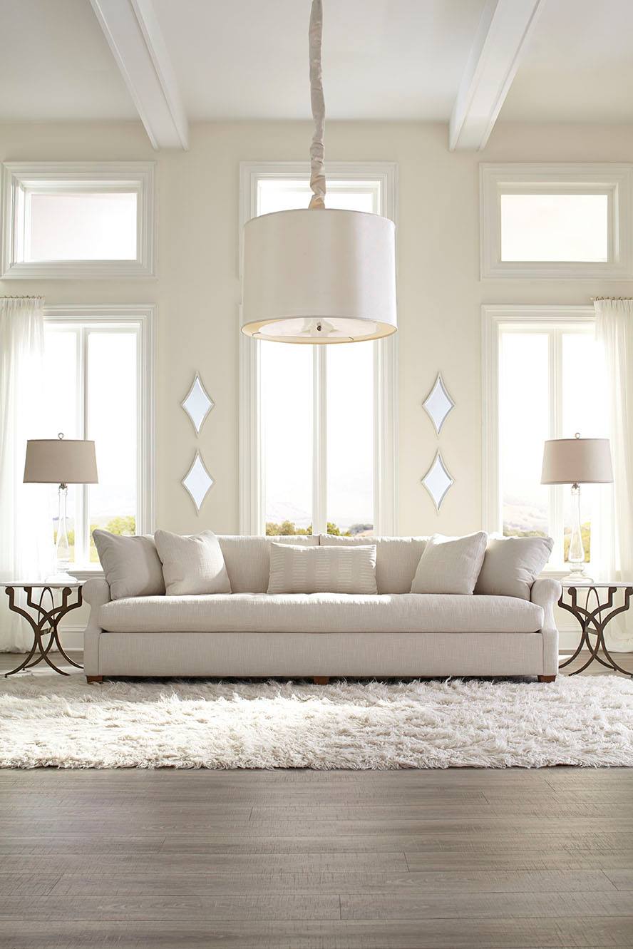 Living room with white sofa, rug, and large windows. Neutral colors, lamps and pendant light.