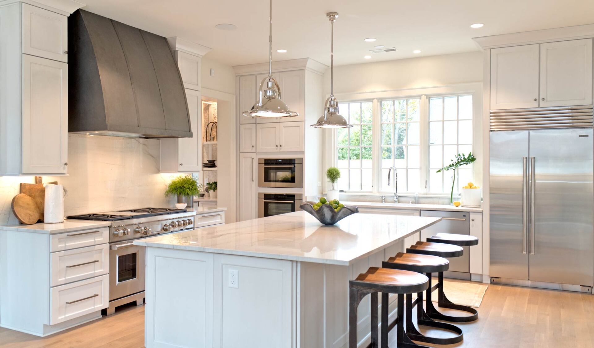 Modern white kitchen with island, stainless steel appliances, and pendant lights.