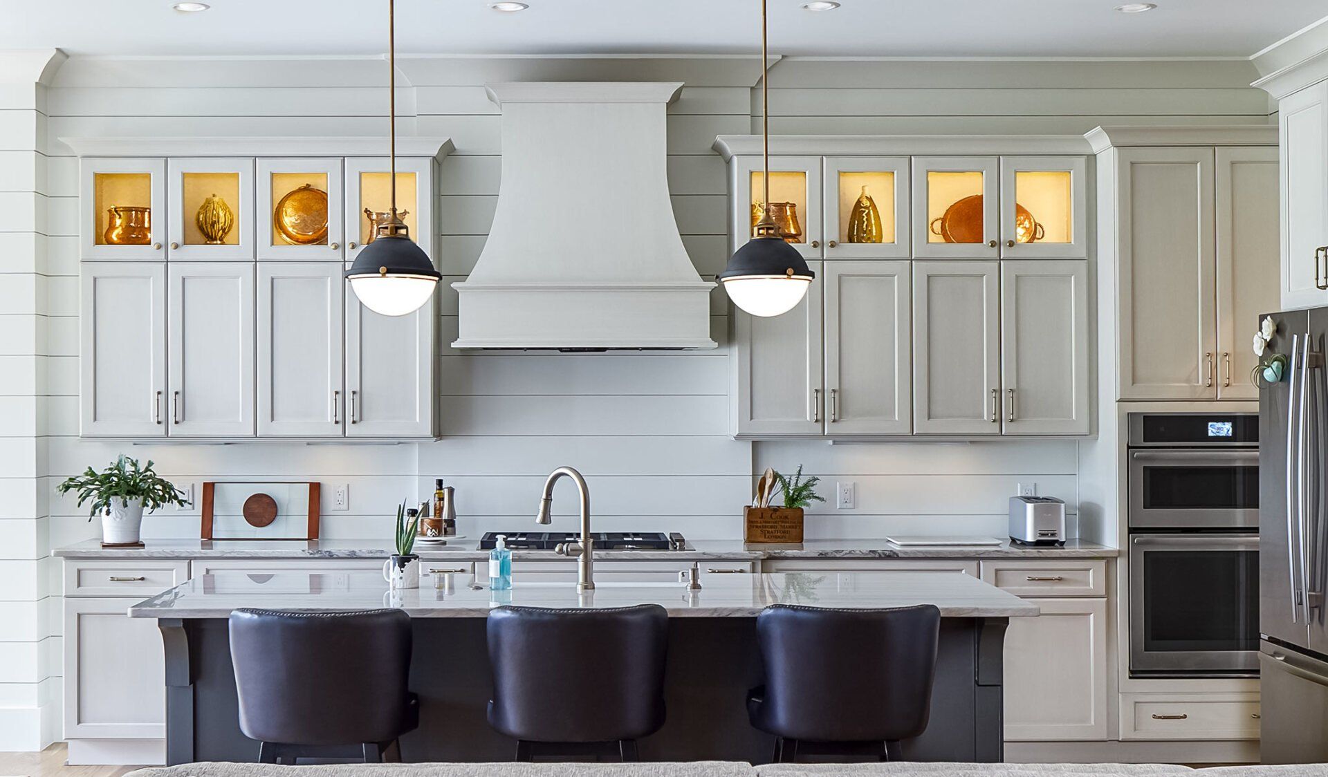 Modern kitchen with white cabinets, black island, pendant lights, and stainless steel appliances.