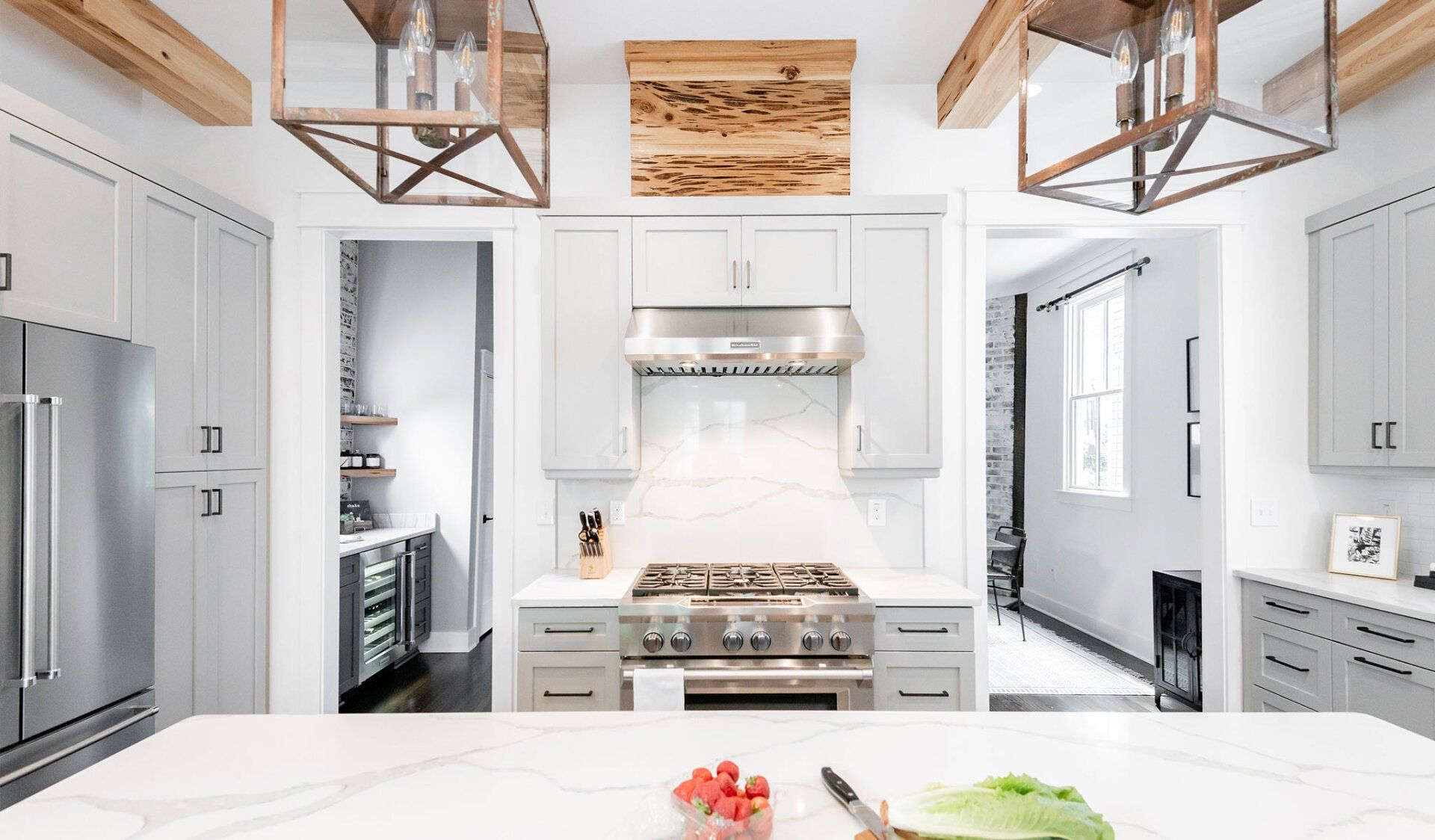Modern white kitchen with stainless steel appliances, wooden accents, and a large island with food.