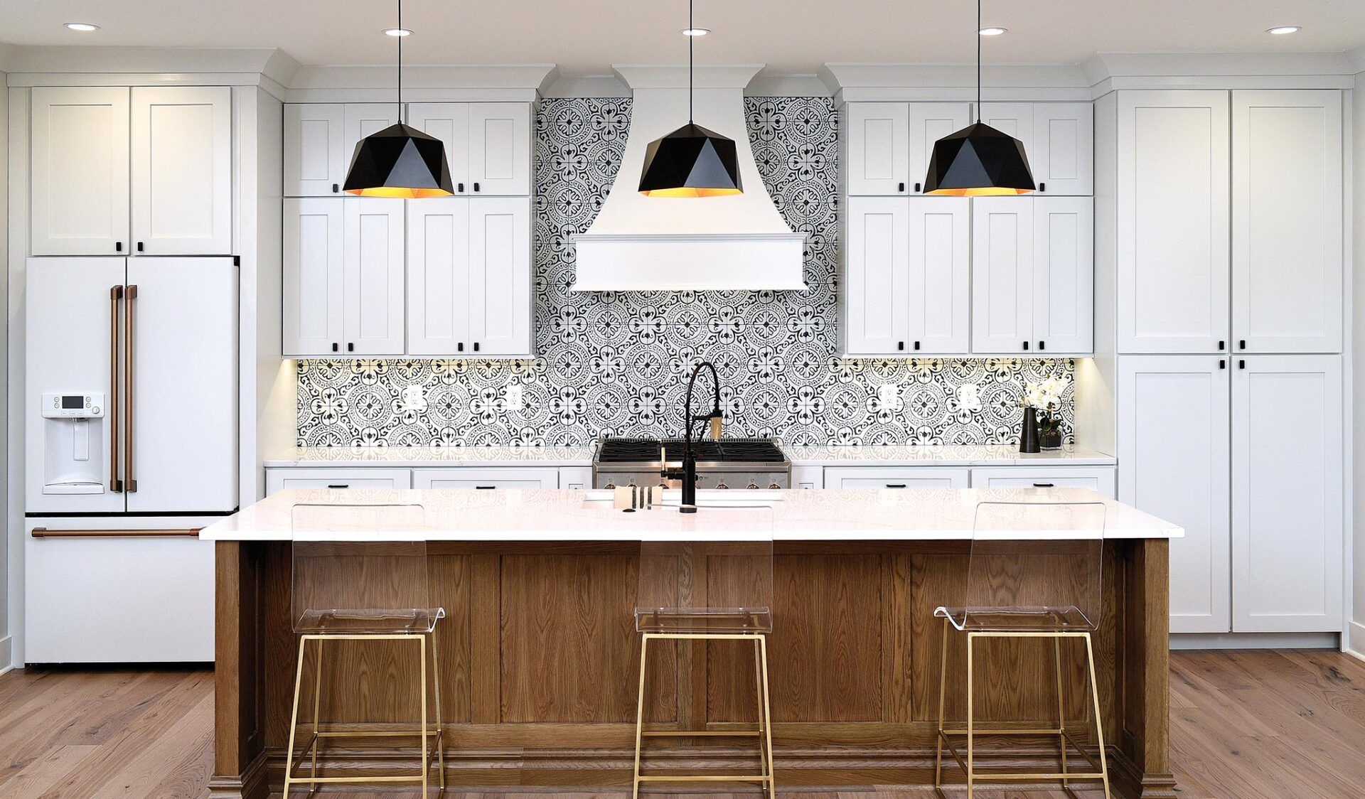 Modern white kitchen with island, wood cabinets, gold accents, black light fixtures, and mosaic backsplash.