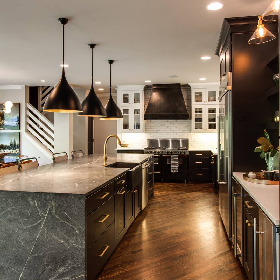 Modern kitchen with dark cabinets, gold accents, and three black pendant lights over a gray island.