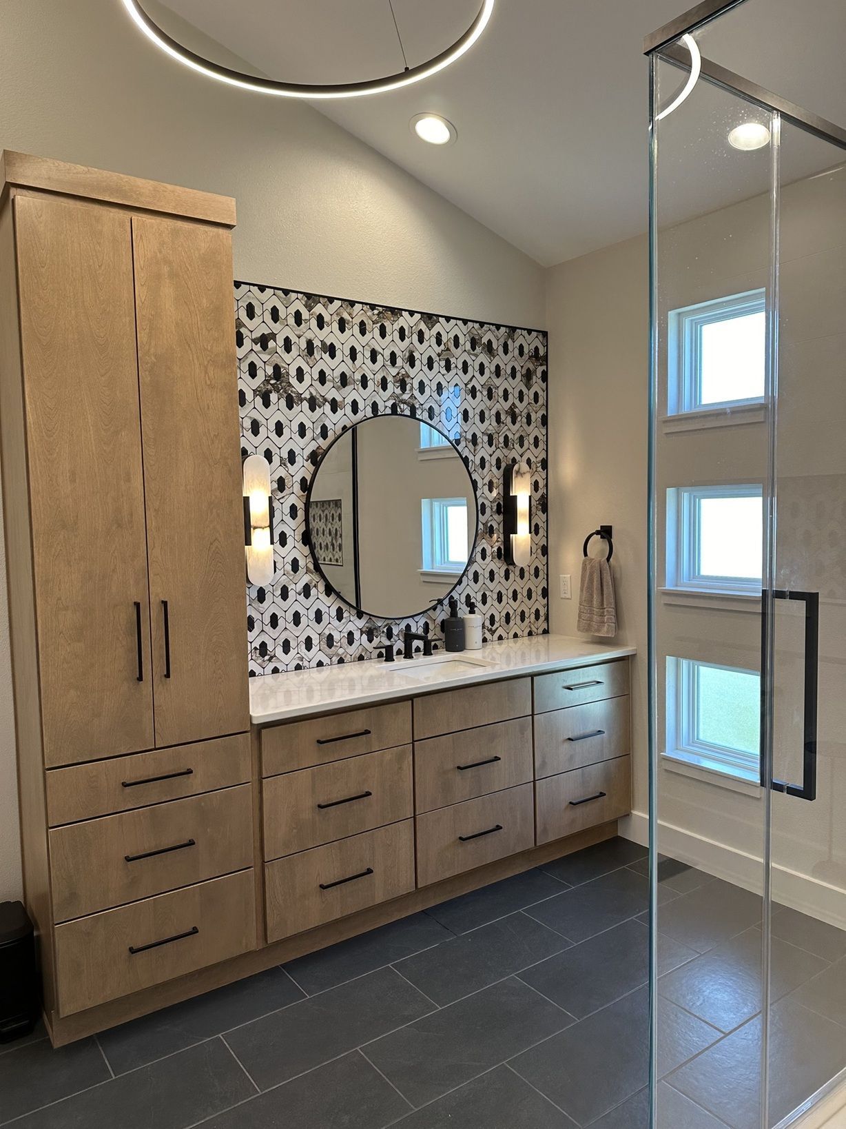 A bathroom with a sink , mirror , cabinets and a walk in shower.