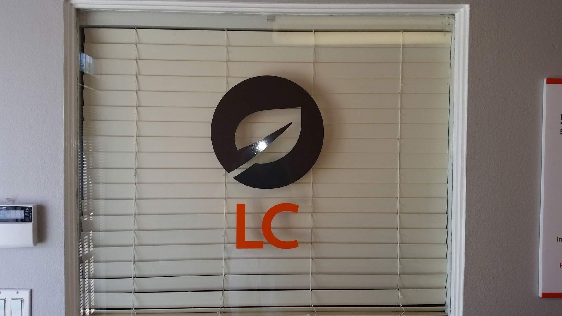 A window with blinds and a logo that says LC