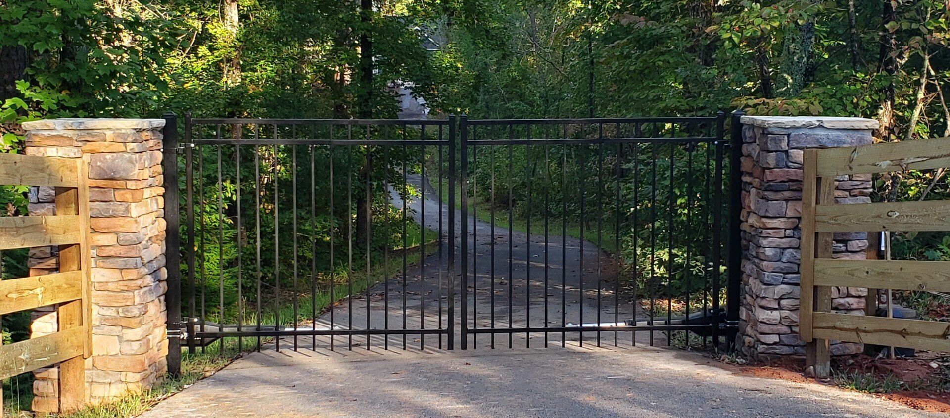 A metal gate is open to a dirt road surrounded by trees.