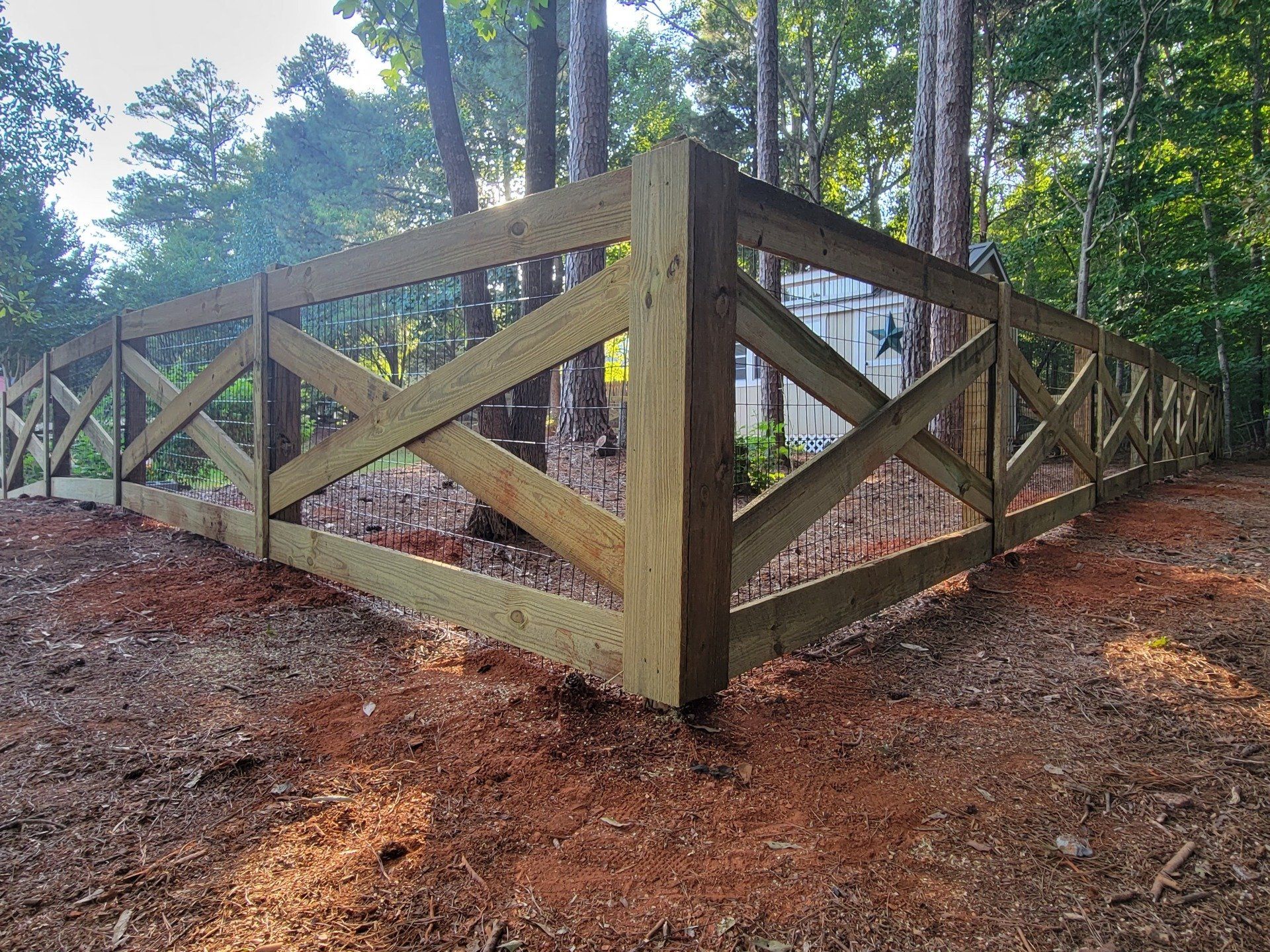 A wooden fence surrounds a dirt path in the woods.