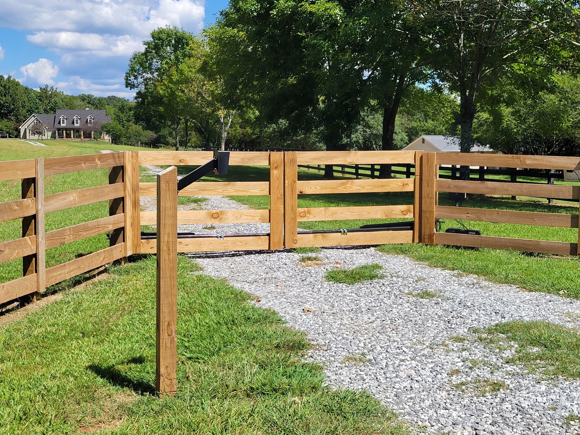 A wooden fence with a gate in the middle of a grassy field.