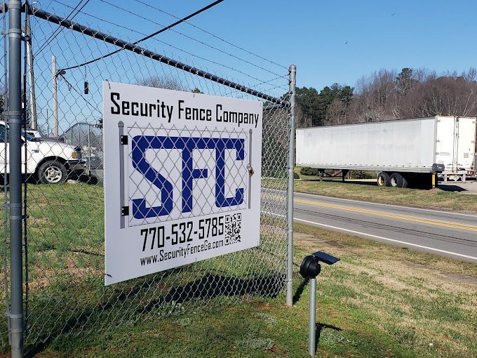 A sign on a chain link fence says security fence company sfc