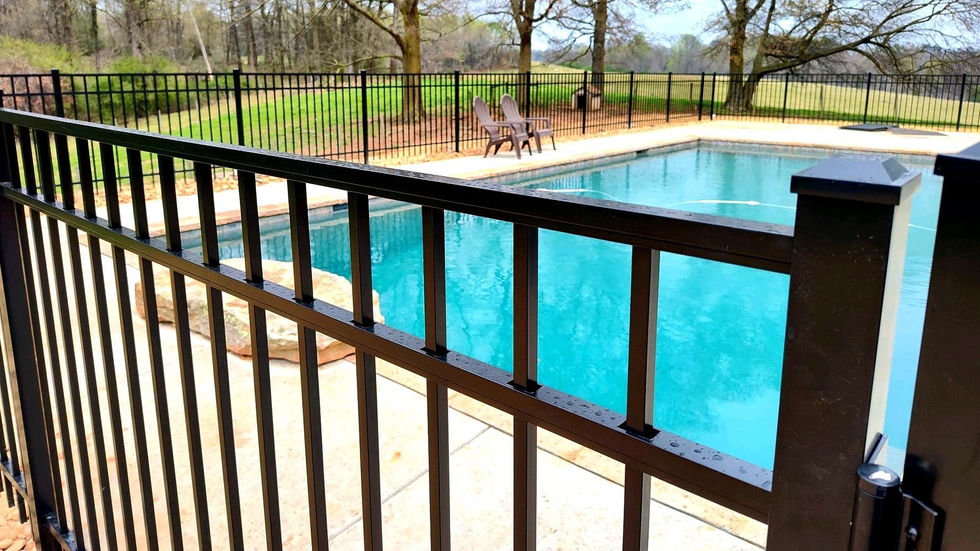 A black fence surrounds a large swimming pool.