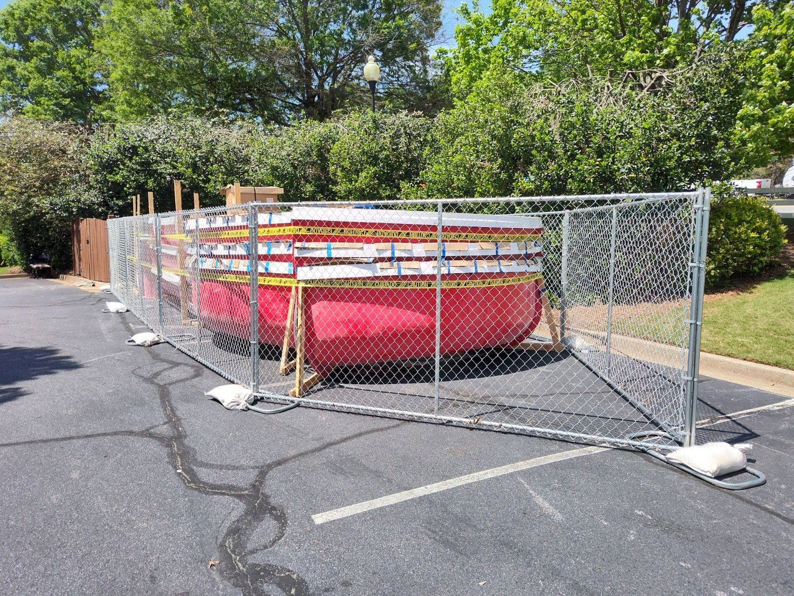 A red dumpster is behind a chain link fence in a parking lot.