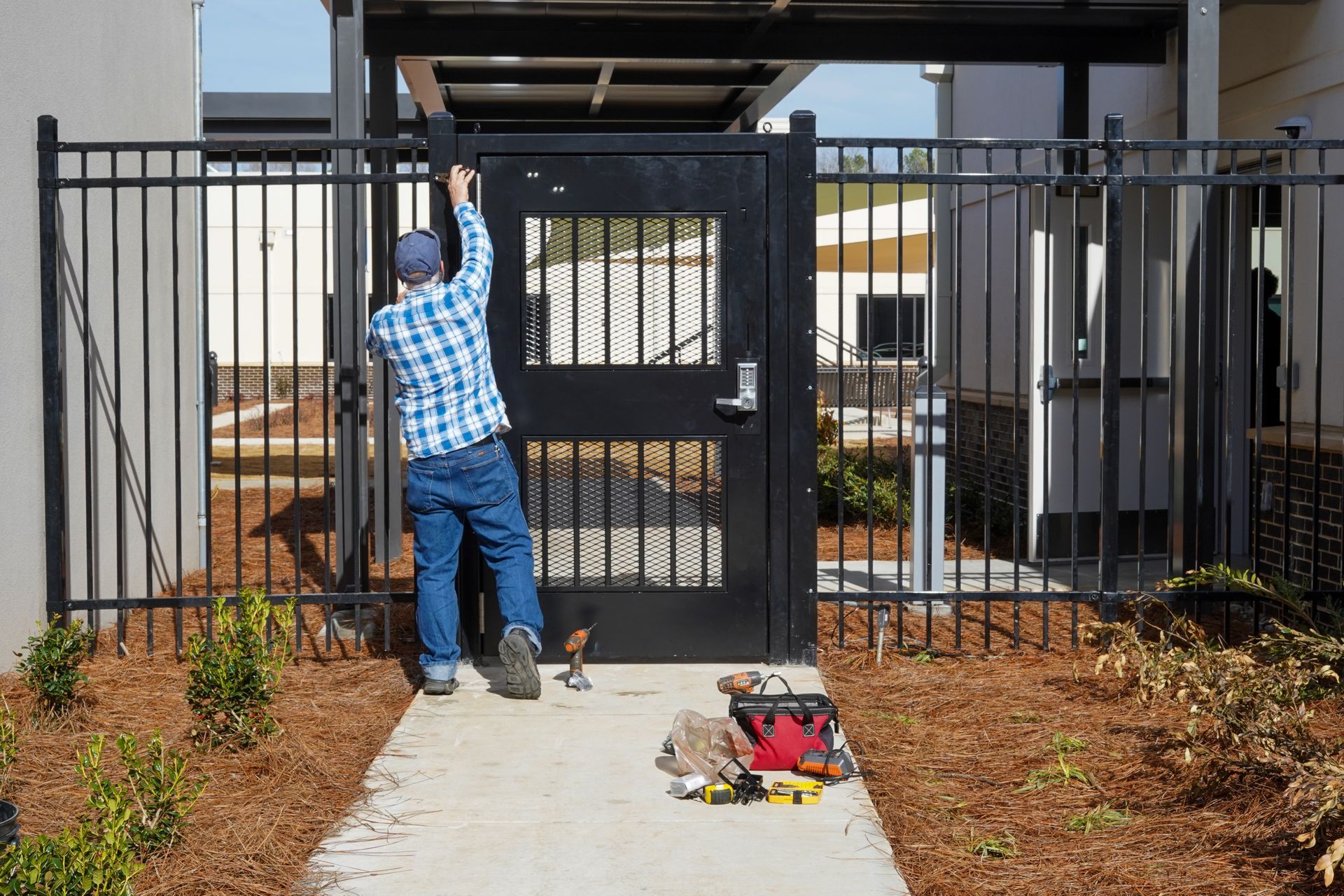 A man is fixing a gate on a sidewalk.