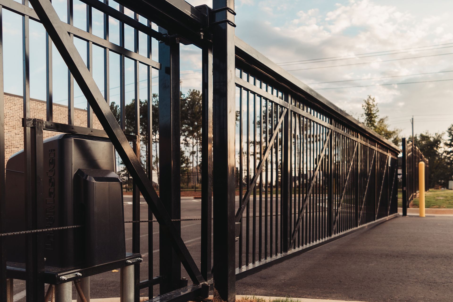 A black sliding gate is open to a parking lot.