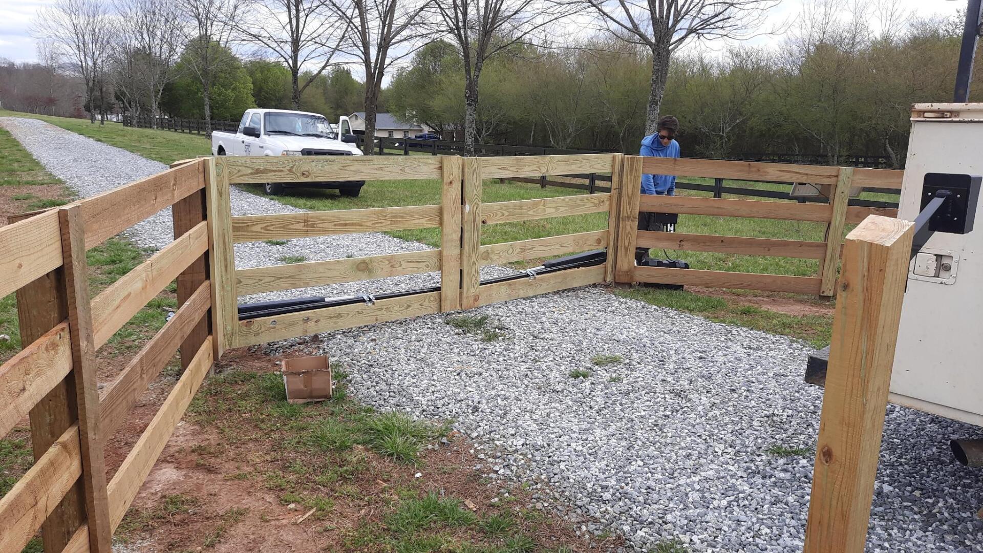 A man is standing behind a wooden fence next to a gravel road.