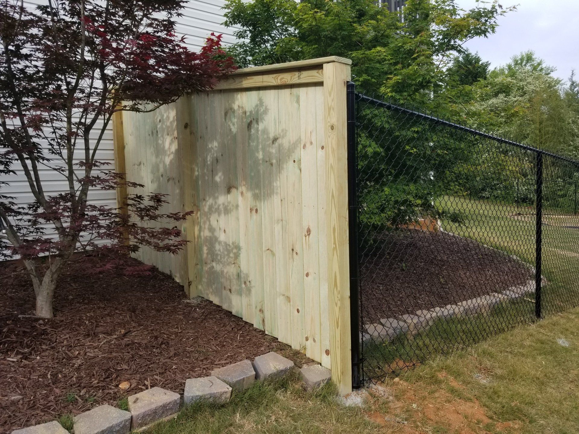 A wooden fence with a chain link fence in front of a house.