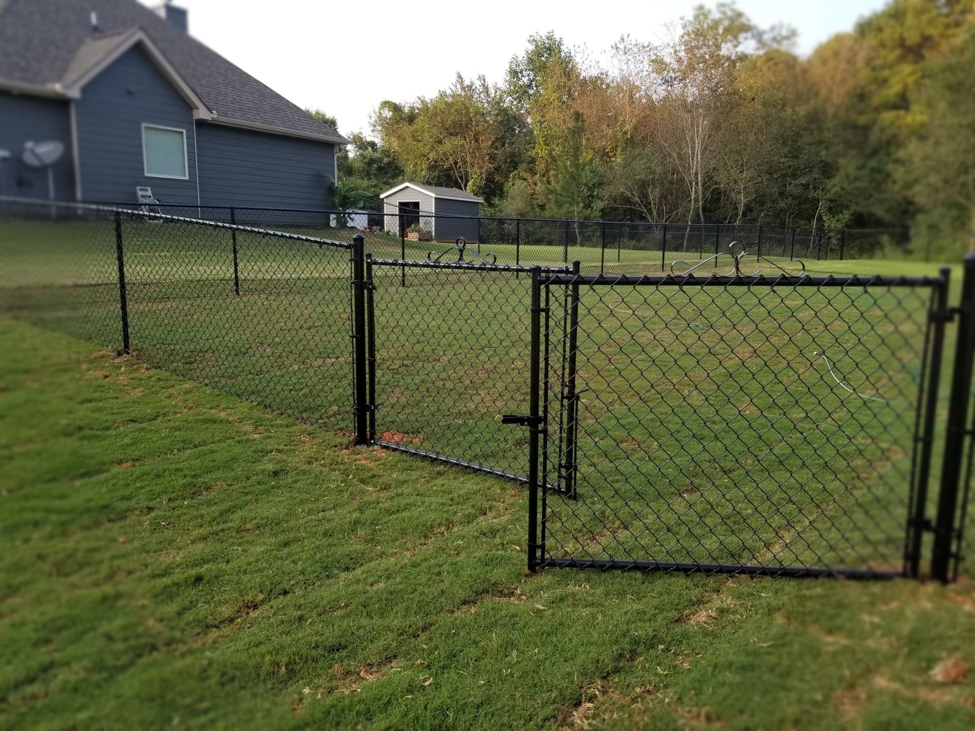 A chain link fence with a gate in the middle of a lush green field.