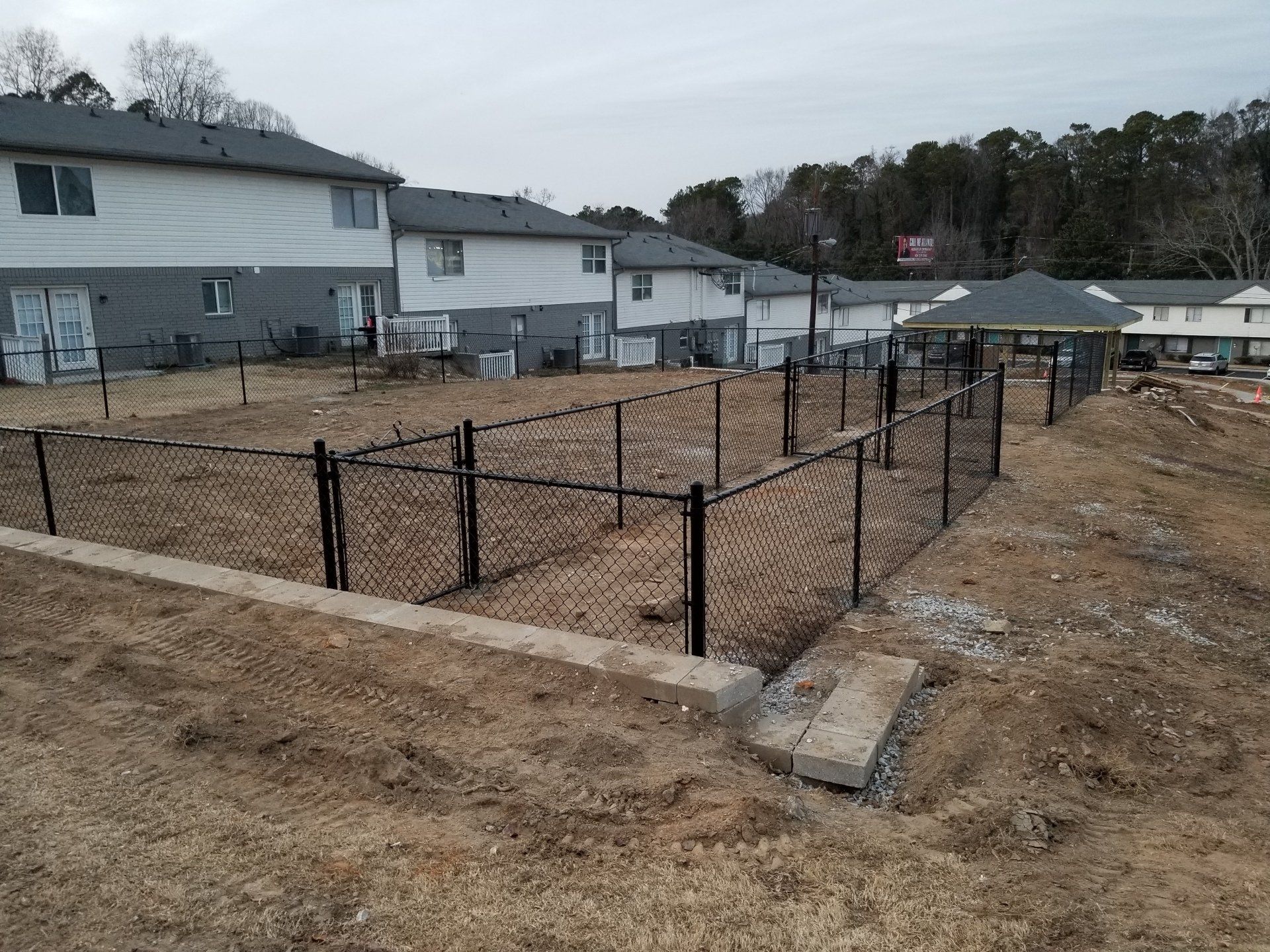 A chain link fence surrounds a dirt field in front of a building.