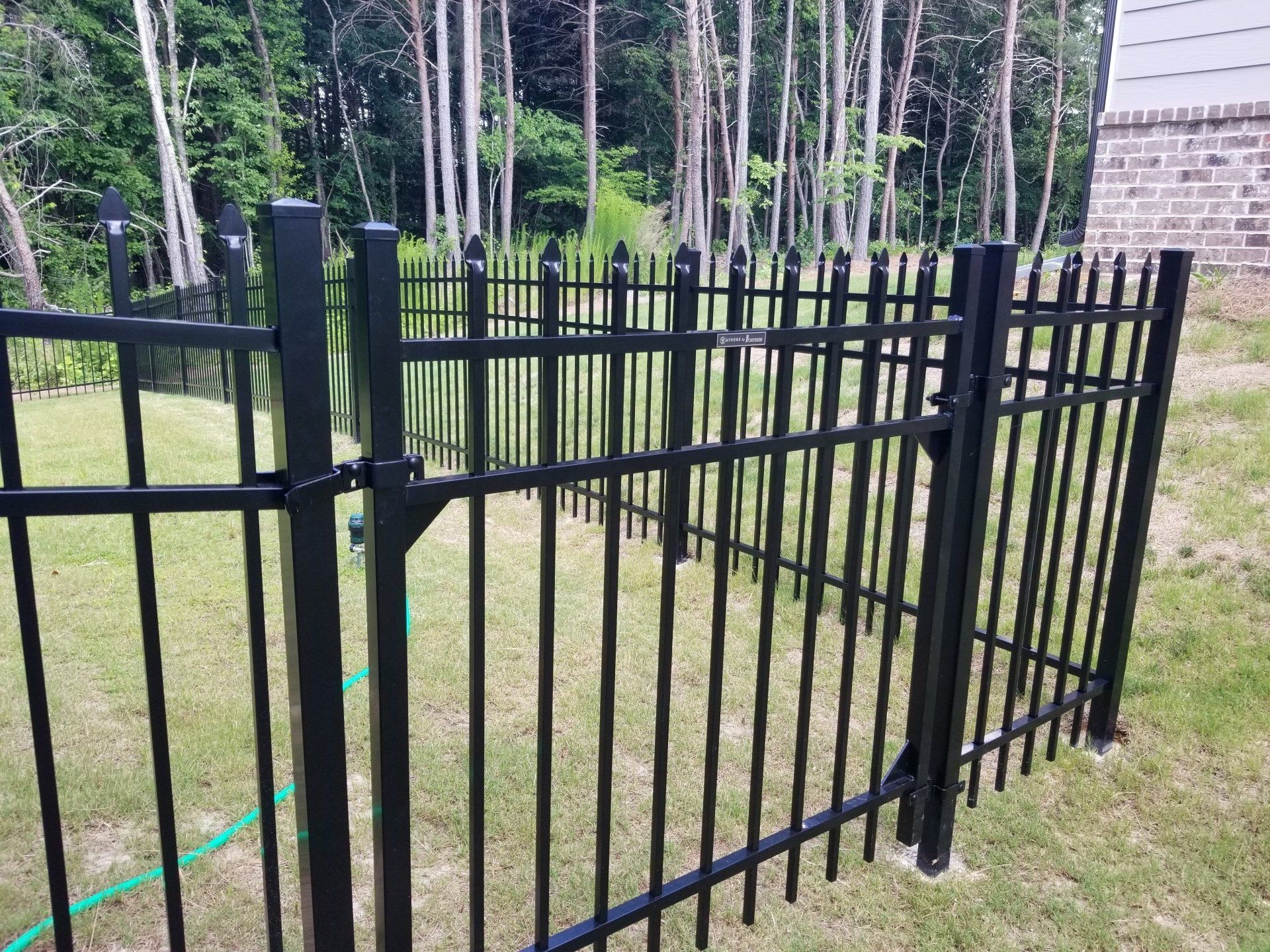 A black metal fence is surrounding a lush green yard.