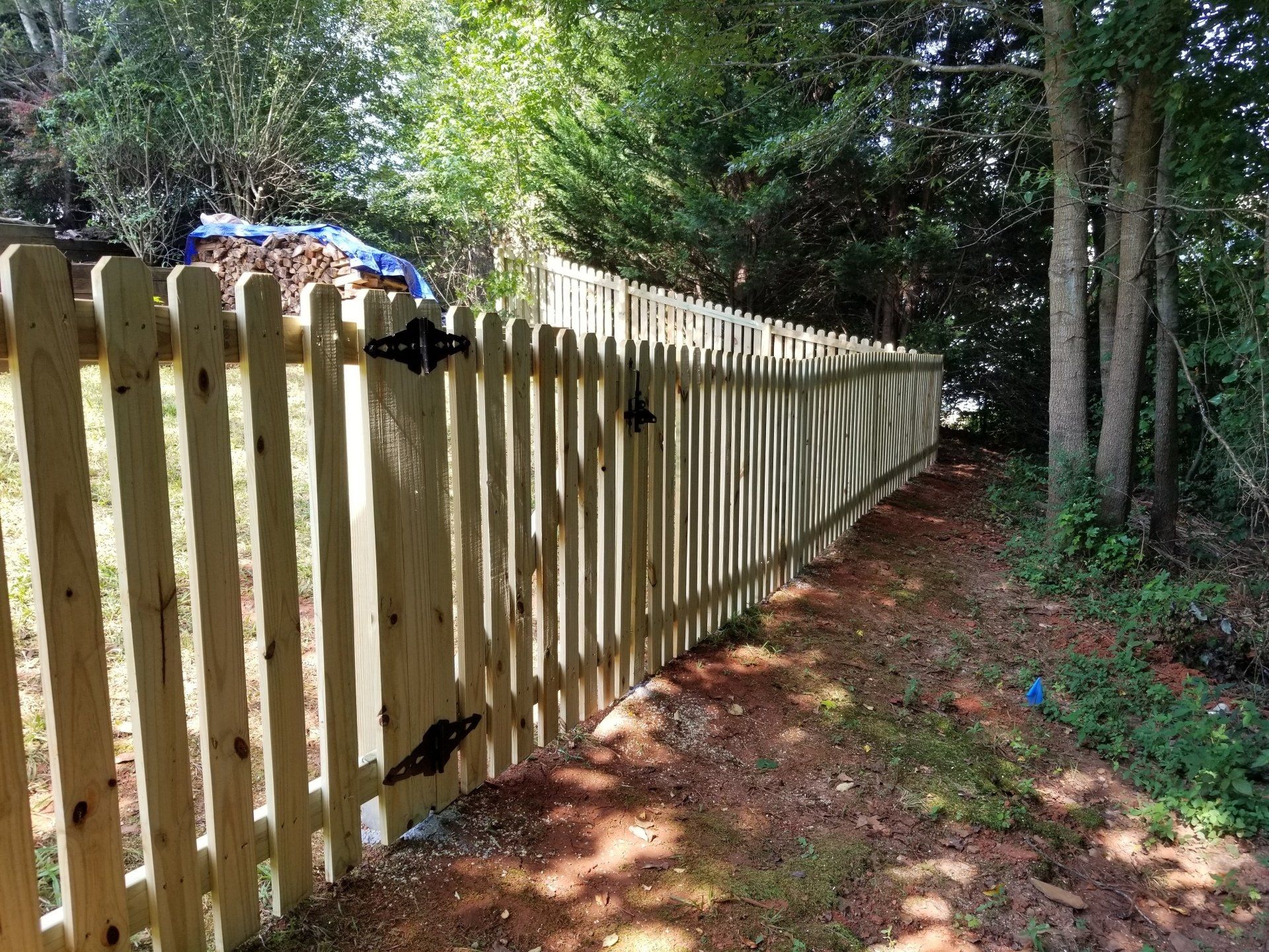 A wooden picket fence surrounds a dirt path in the woods.