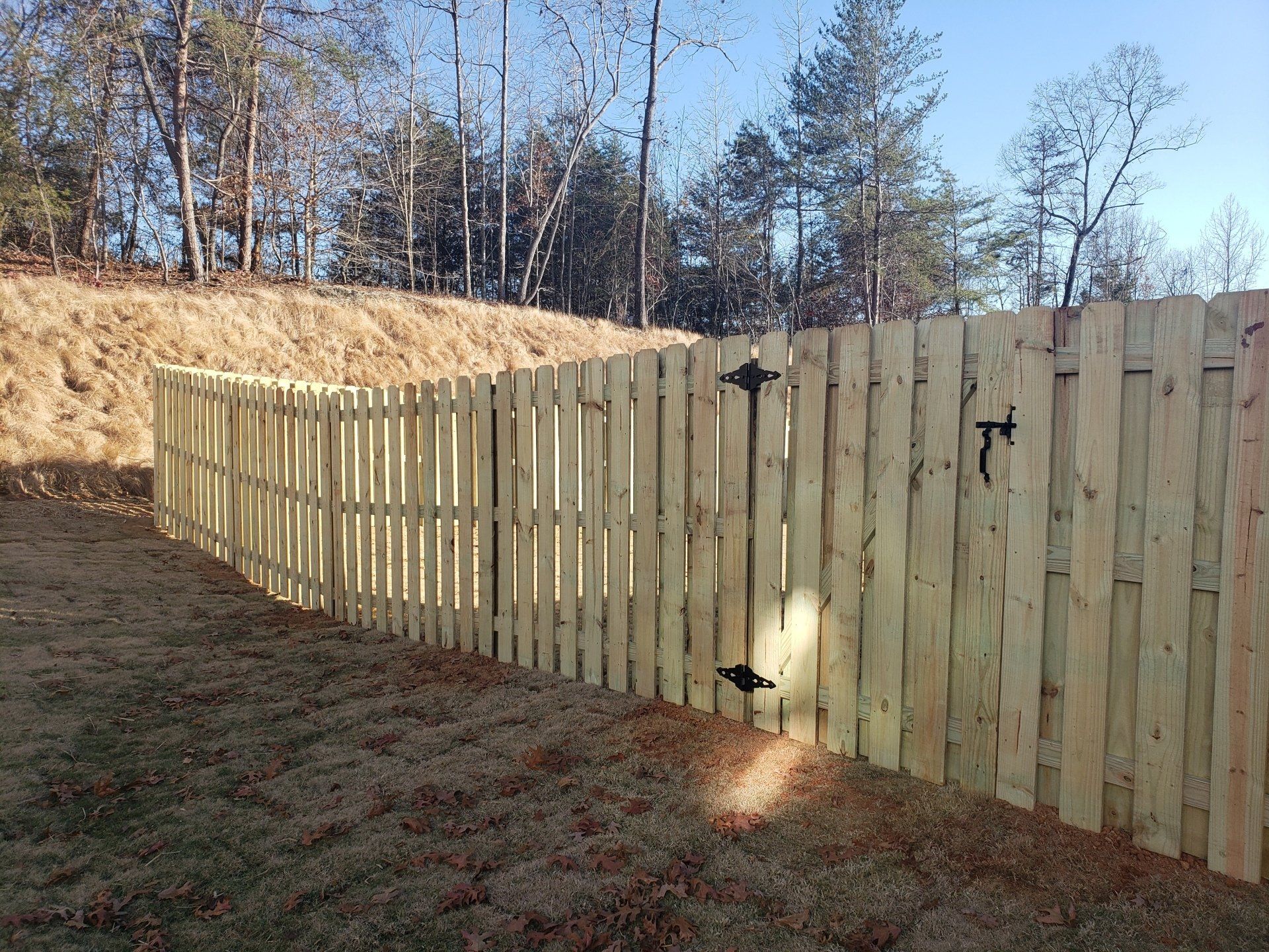 A wooden fence with a gate is surrounded by grass and trees.
