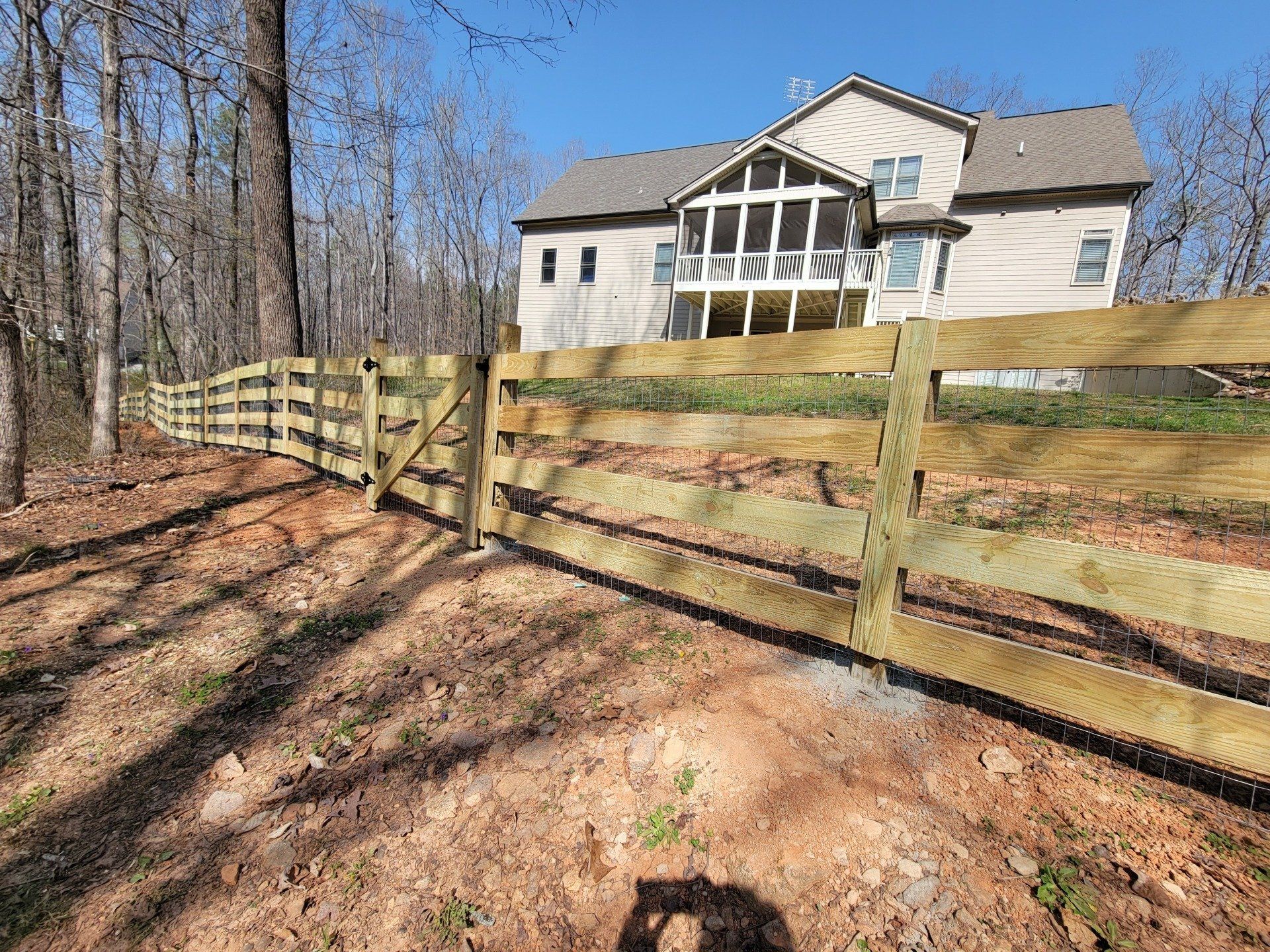 A wooden fence surrounds a large house in the woods.