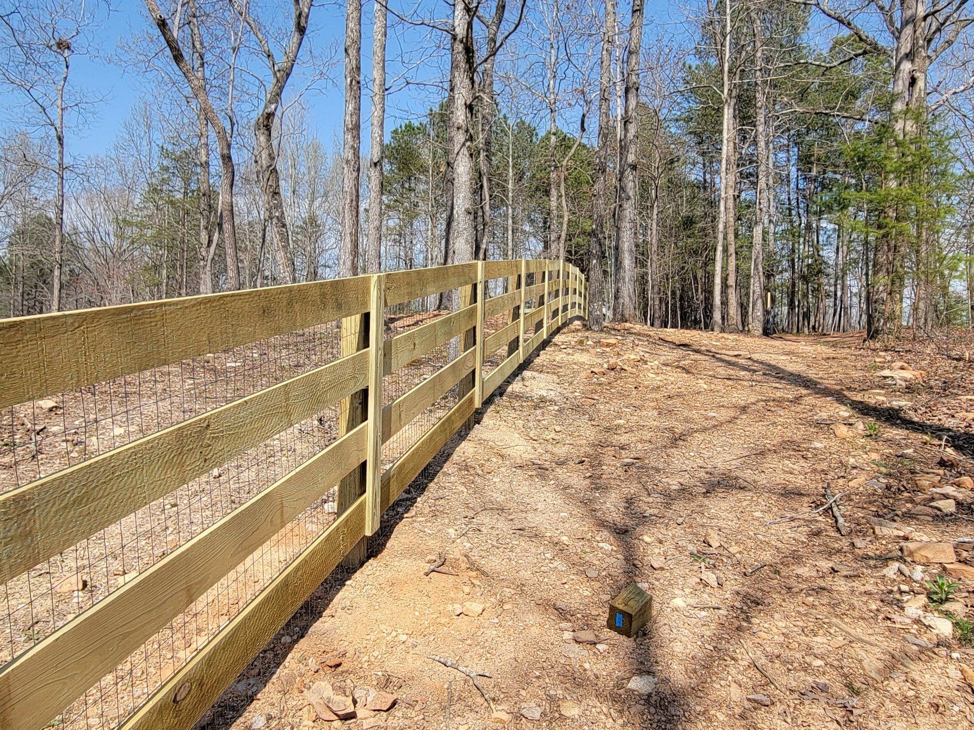 A wooden fence surrounds a dirt path in the woods.