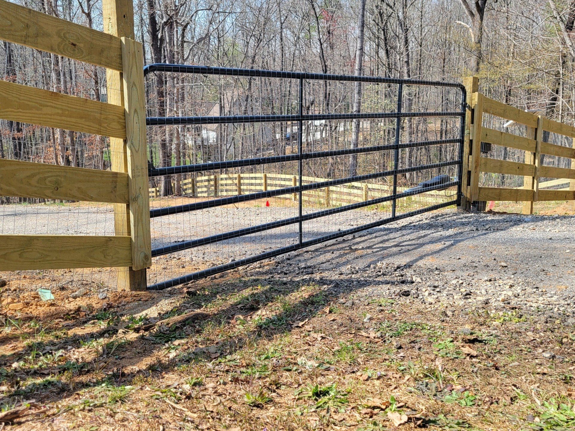 A wooden fence with a metal gate in the middle of a dirt road.