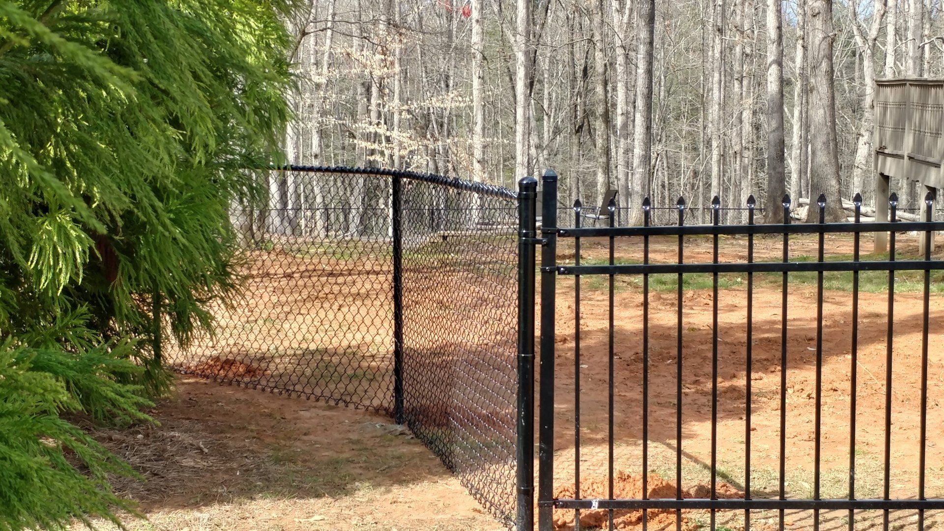 A chain link fence surrounds a dirt field with trees in the background.