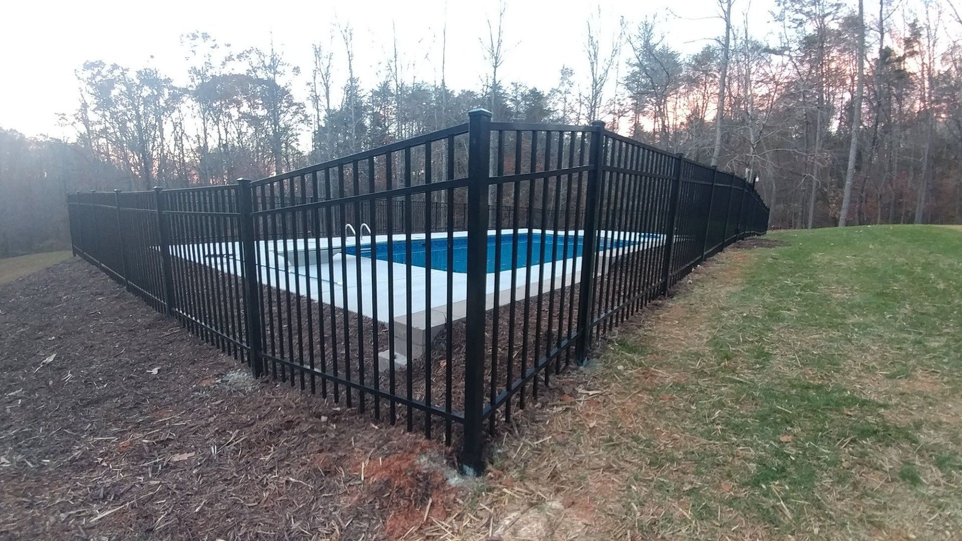 A black fence surrounds a swimming pool in a backyard.