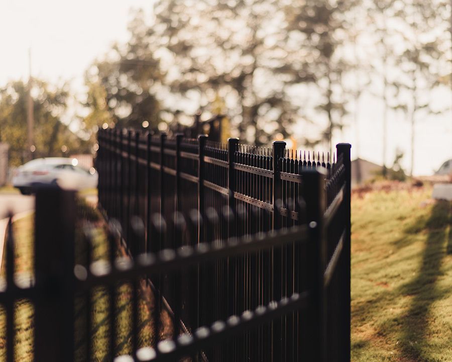 A close up of a black fence with trees in the background.
