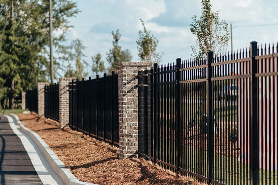 A black metal fence with brick pillars along the side of a road.