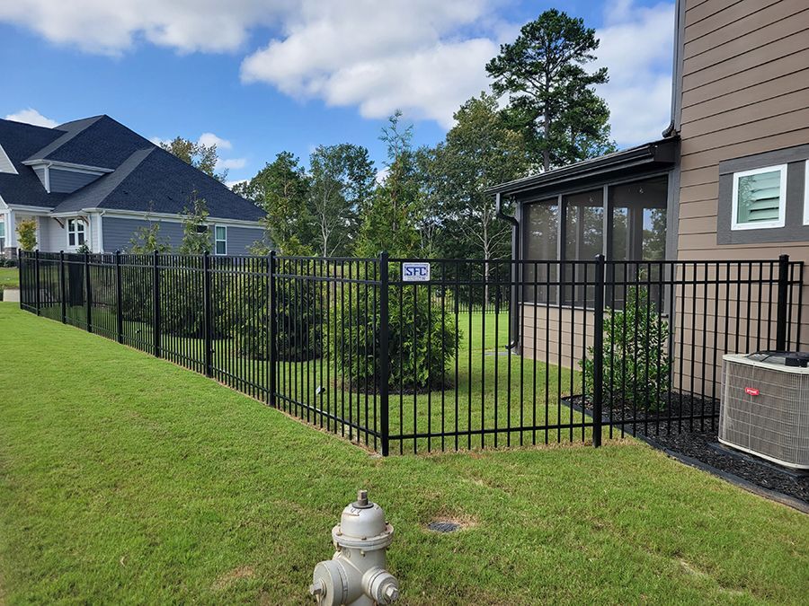 A fire hydrant is in the grass next to a fence in front of a house.