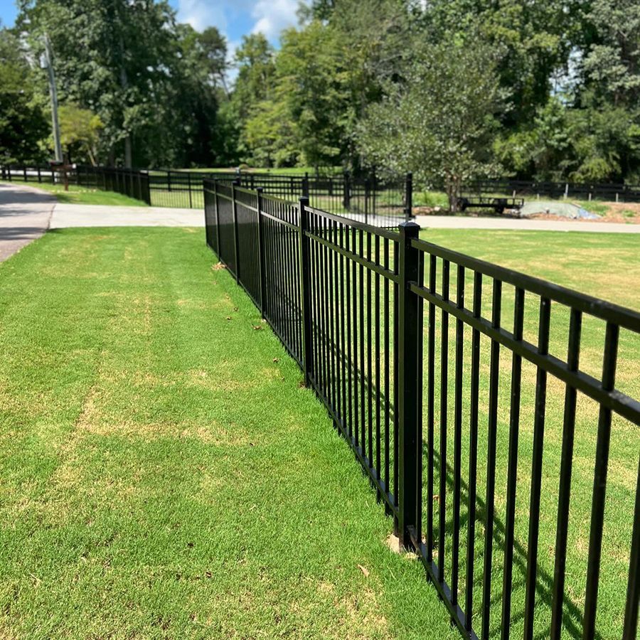 A black metal fence surrounds a lush green field.