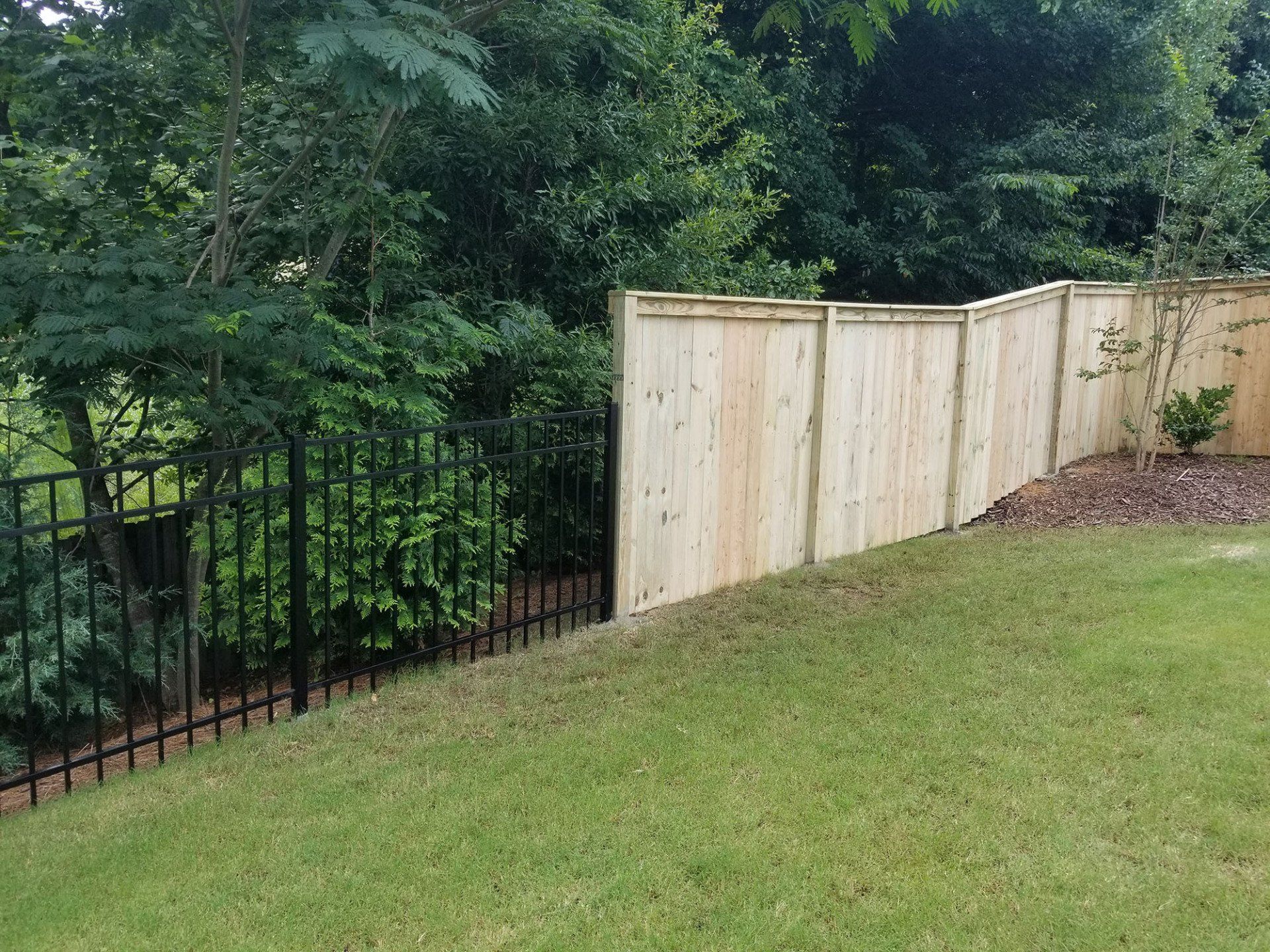 A wooden fence with a black fence surrounding it in a backyard.