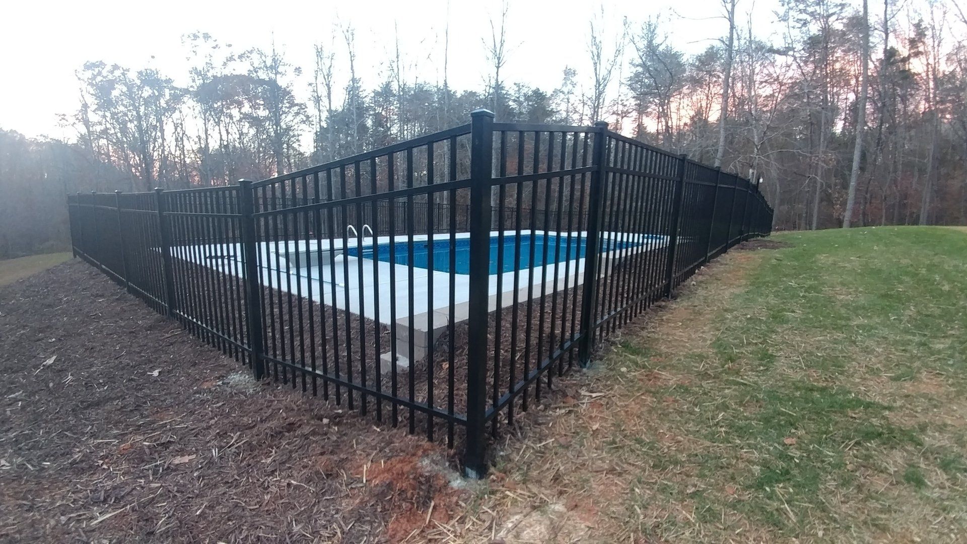 A black fence surrounds a swimming pool in a backyard.