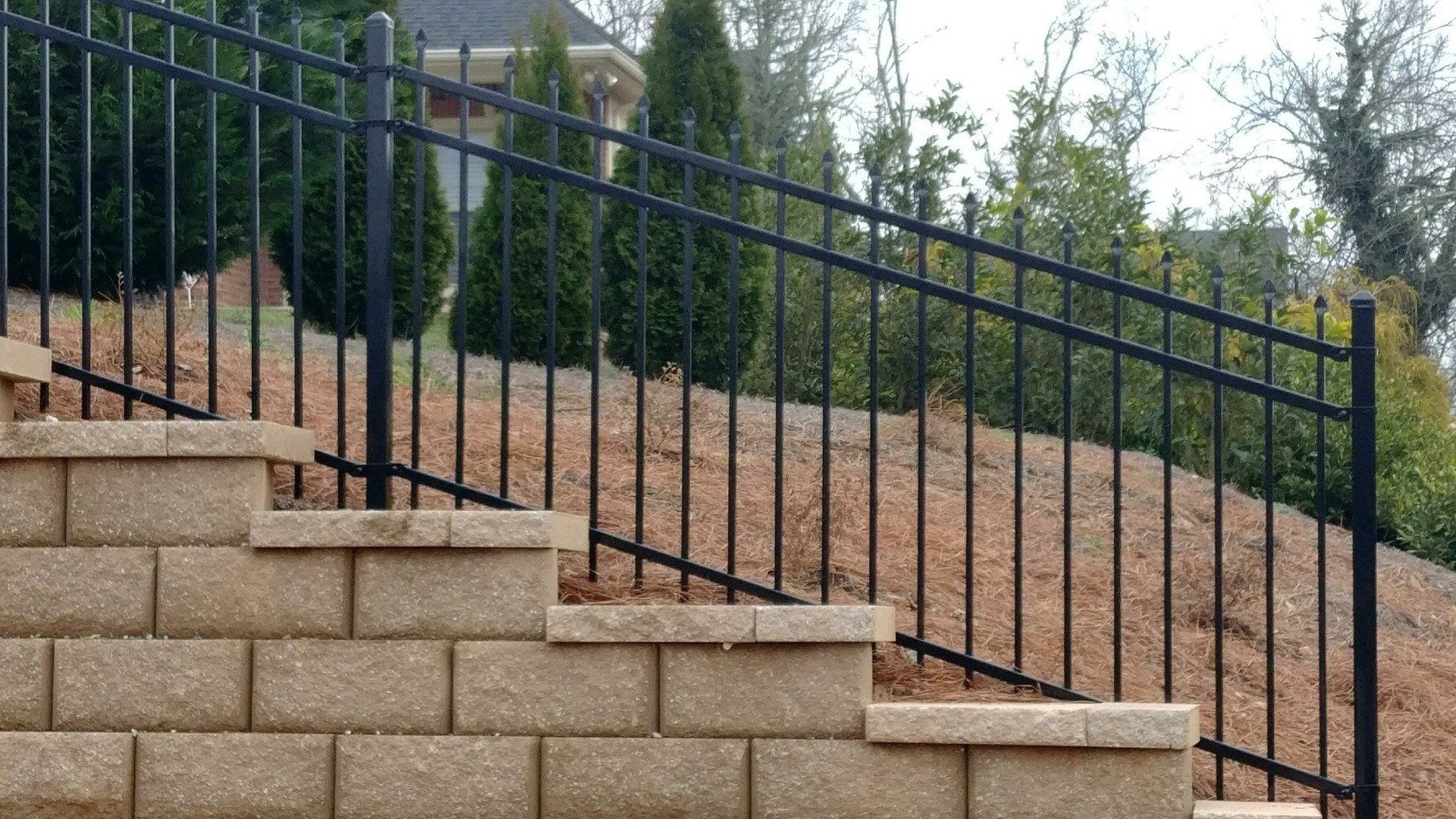 A wrought iron fence surrounds a brick wall and stairs leading up to a house.